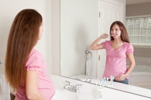 A beautiful pregnant woman looking into a mirror as she brushes her teeth.